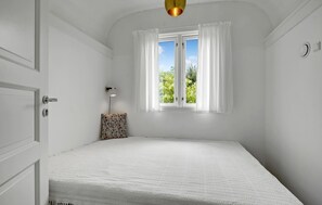 Ein Zimmer mit einem Bett, einem Vorhangfenster, einer Wandleuchte und einer Tür.