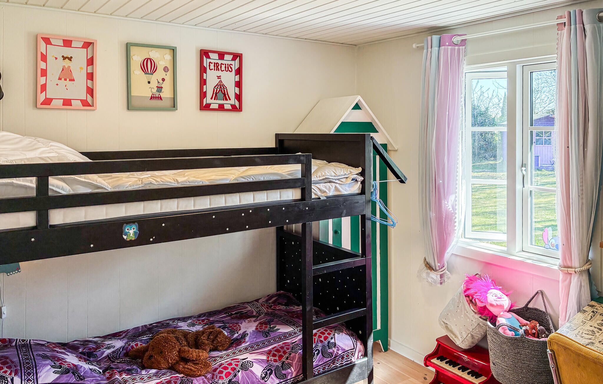 Een slaapkamer met stapelbed, raam, een klein piano en wanddecoraties.