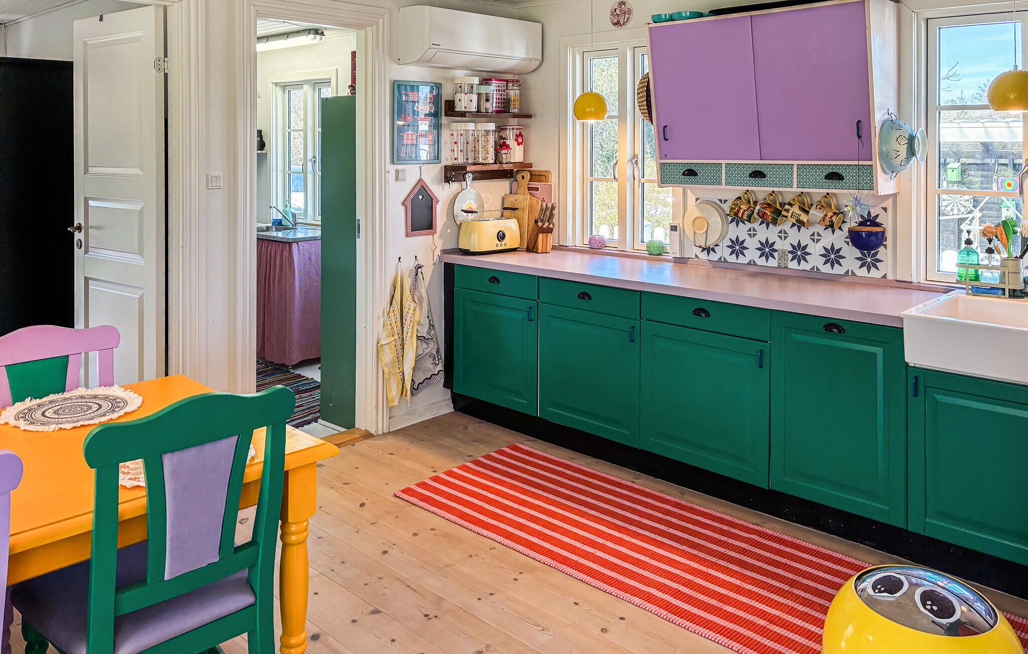 A kitchen with green cabinets, a yellow toaster, and a red striped rug.