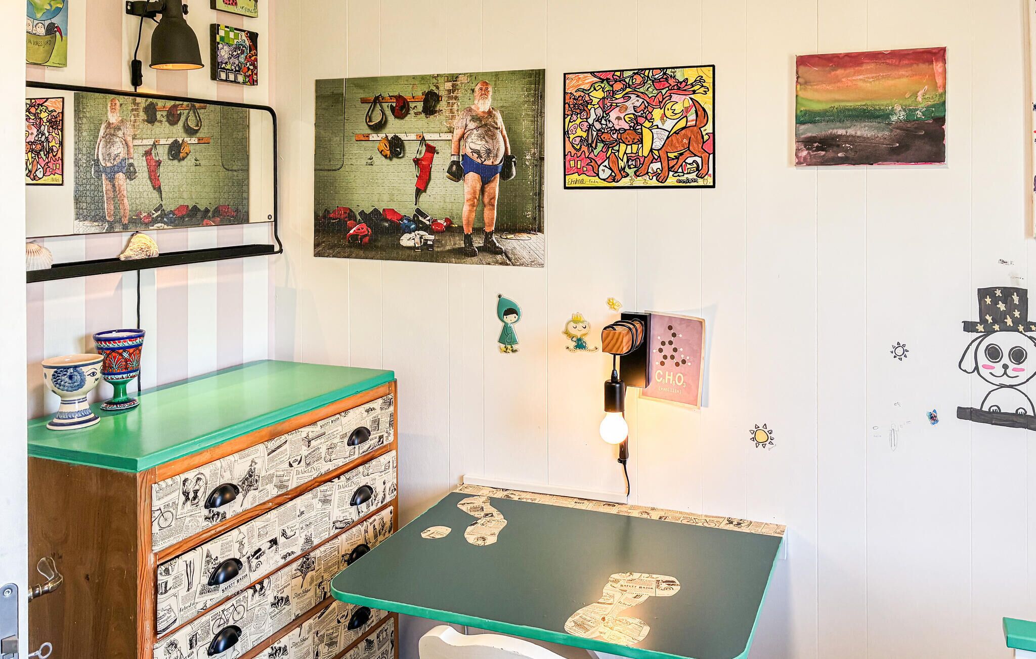 A room with a green table, a wall-mounted shelf with shoes, and various artworks.