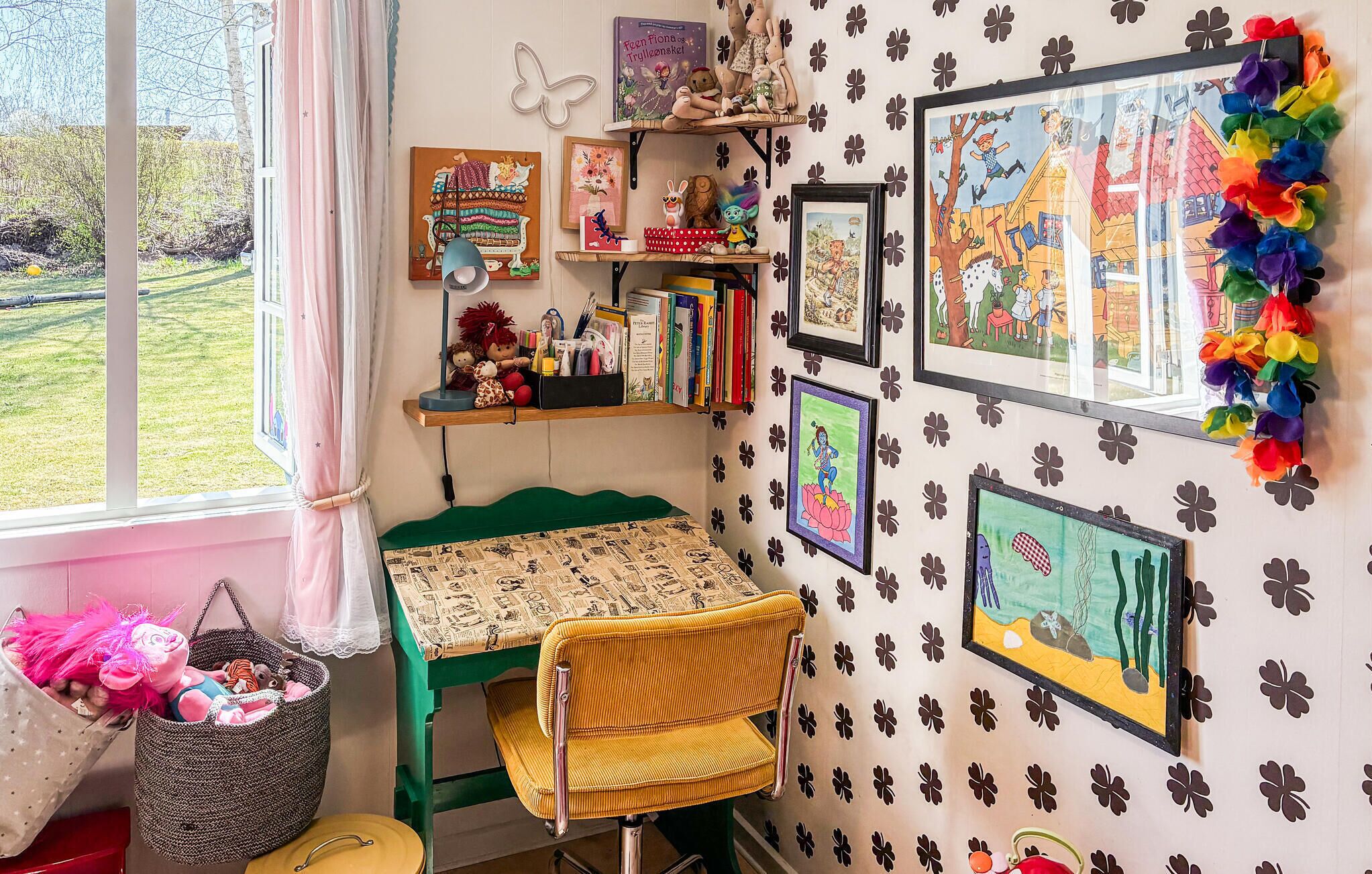 Una habitación infantil con una mesa verde, una silla de mimbre y varios libros y juguetes para niños.