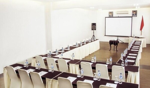Una sala de conferències amb taules llargues, cadires i una pantalla de projector.