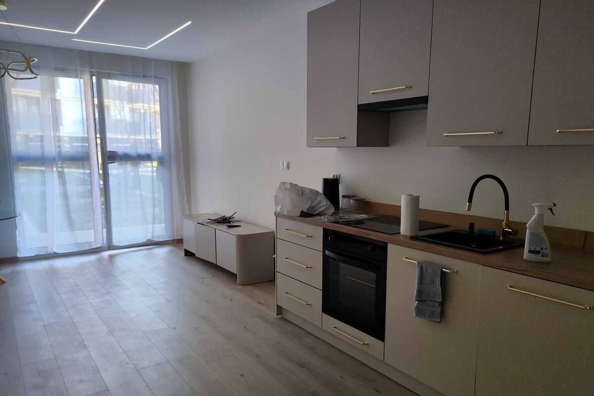 A modern kitchen with a built-in oven, a sink, and a window overlooking a balcony.