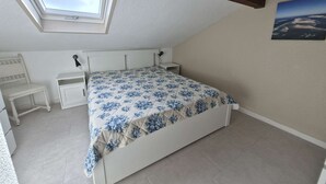 Ett sovrum med ett takfönster, en säng med ett blommigt överkast, ett sängbord, en stol och ett litet skrivbord.
