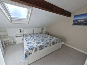 A bedroom with a skylight, a bed with a floral bedspread, a bedside table, a chair, and a small desk. - Charming apartment ideal for 4 people, perfect for a comfortable stay between ocean and... (BISCARROSSE PLAGE)