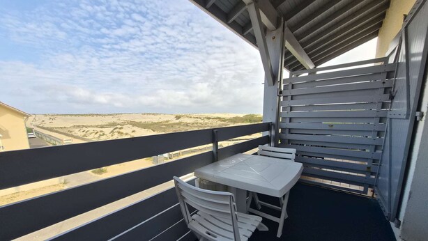 En balkong med ett bord och några stolar, med utsikt över ett sandigt landskap.