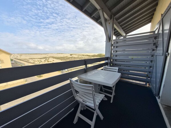 A balcony with a table and chairs, overlooking a sandy landscape. - Charming apartment ideal for 4 people, perfect for a comfortable stay between ocean and... (BISCARROSSE PLAGE)