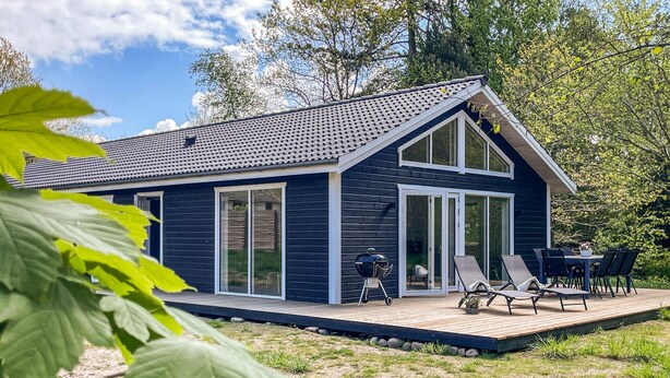 Et moderne hus med stor terrasse, skydedøre og en patio med udendørs møbler.