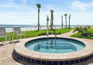 A pool area with a view of the ocean, surrounded by palm trees and lounge chairs. - Spacious Upscale 3BR Condo Balcony Ocean View & Steps to Beach (Daytona Beach)