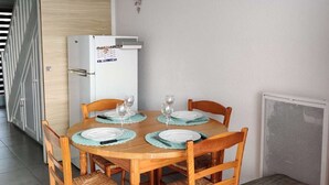 Ein Essbereich mit einem Holztisch, gedeckt für vier Personen, umgeben von Korbstühlen, einem weißen Kühlschrank und einer Heizung.
