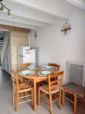 Ein Essbereich mit einem Holztisch, gedeckt für vier Personen, umgeben von Korbstühlen, einem weißen Kühlschrank und einer Heizung.