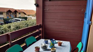 Ein Balkon mit karierter Tischdecke, grünen Stühlen sowie verschiedenen Tassen und einem Teekessel.