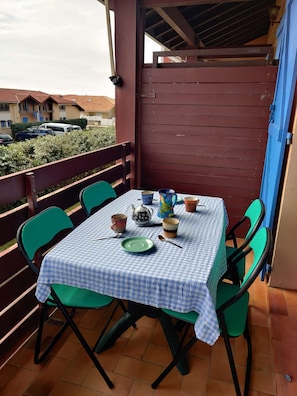 Ein Balkon mit karierter Tischdecke, grünen Stühlen sowie verschiedenen Tassen und einem Teekessel.