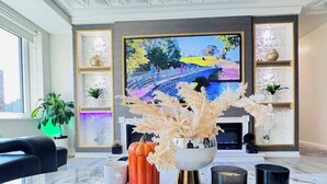 A modern living room with a marble coffee table, a flat-screen TV, decorative plants, and a fireplace.