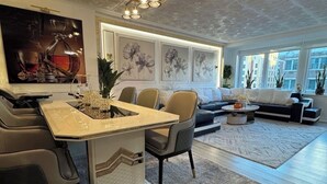 A modern living room with a dining area, large windows, and decorative wall art.