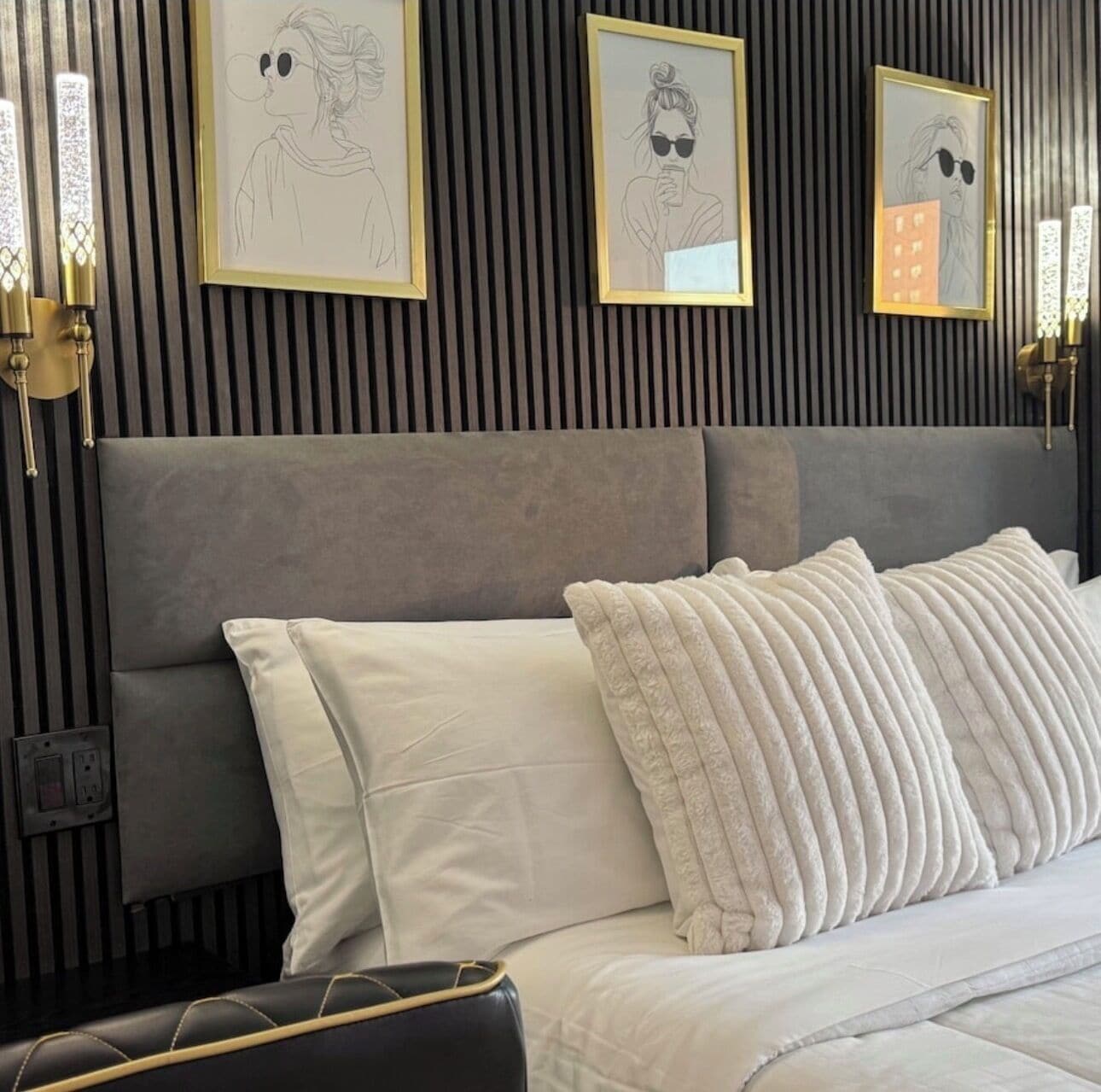 A bedroom with a grey upholstered headboard, white bedding, and framed artwork on the wall.