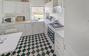 Pieni, käytännöllinen keittiö, jossa on valkoiset kaapit, ruutukuviollinen lattia, ikkuna ja perusvarusteet.