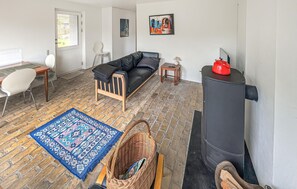 A living room with a black sofa, a patterned rug, a wooden chair, a small table with a lamp, and a black stove. - 3 bedroom gorgeous home in Kalundborg (Kalundborg)