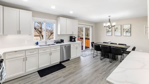A modern kitchen with white cabinets, a dishwasher, and a dining area with a table and chairs. - Finally… A Home Big Enough for Everyone 8 Beds (Woodstock)