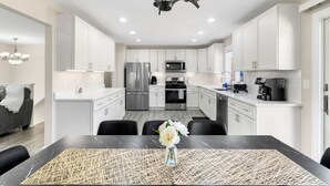 A modern kitchen with white cabinets, stainless steel appliances, and a dining area with a black table and chairs. - Finally… A Home Big Enough for Everyone 8 Beds (Woodstock)