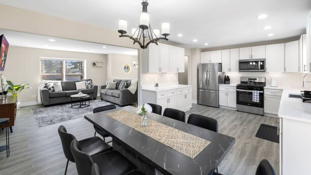 A modern kitchen with stainless steel appliances, a dining area with a marble table, and a living room with a grey sofa. - Finally… A Home Big Enough for Everyone 8 Beds (Woodstock)