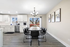 A modern kitchen with white cabinets, a dining area with a long table and black chairs, and a chandelier.