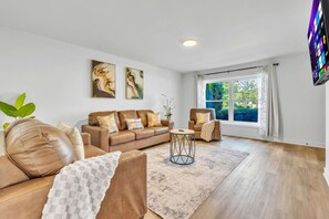 A spacious living room with a leather sofa, a round coffee table, and a large window with curtains. - Spacious Westchester Duplex for Group & Family (Westchester)