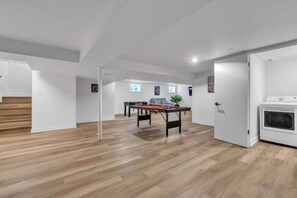 A spacious room with a pool table, a door leading to a laundry area, and a staircase. - Spacious Westchester Duplex for Group & Family (Westchester)