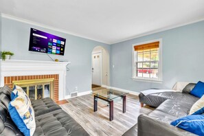 Ein Wohnzimmer mit Kamin, einem an der Wand befestigten Flachbildfernseher und einem Glastisch.