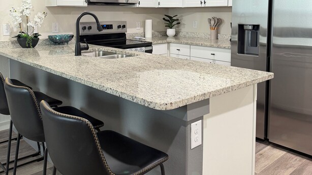 A modern kitchen with white cabinets, a stainless steel refrigerator, a microwave, and a granite countertop. - Modern Stay Near Downtown / Cozy & Clean (San Antonio)