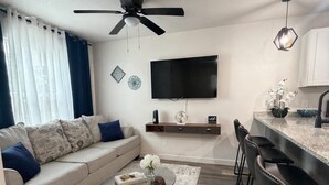 A modern living room with a sofa, coffee table, TV, ceiling fan, and kitchen area with bar stools. - Modern Stay Near Downtown / Cozy & Clean (San Antonio)