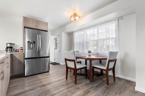 Eine moderne Küche mit einem Edelstahl-Kühlschrank, Holzschränken und einer Essecke mit einem runden Tisch und vier Stühlen.
