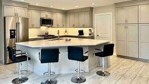 Une cuisine moderne dotée d’un îlot central, d’appareils électroménagers en acier inoxydable et de tabourets de bar.
