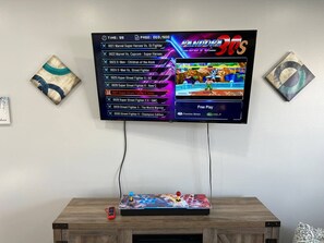 Ein Gaming-Setup mit einem Fernseher, der ein Kampfspiel zeigt, einem Joystick und einer Fernbedienung.