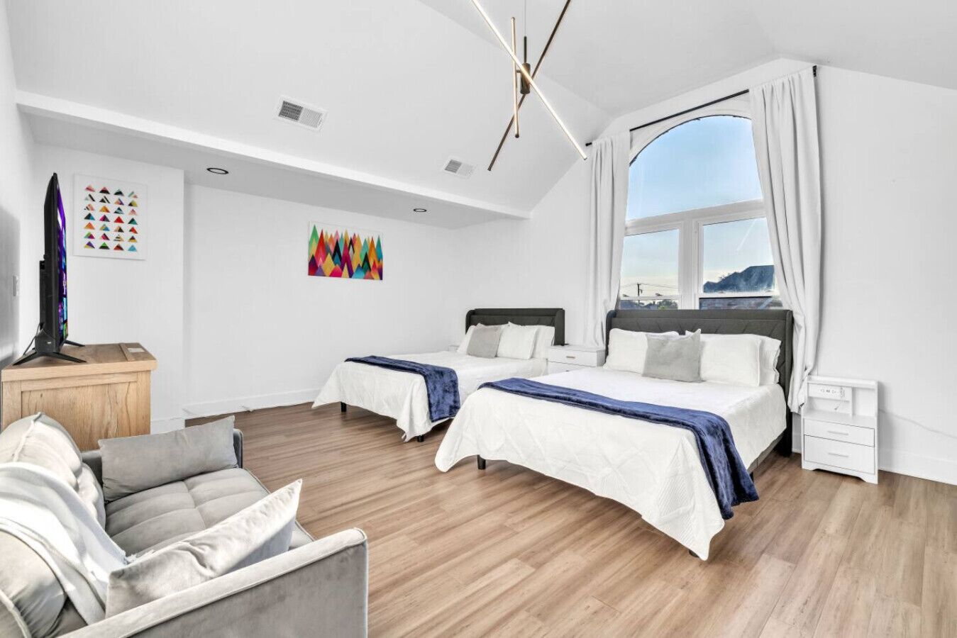 A modern hotel room with two beds, a sofa, a TV, and a large window.