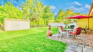 Een achtertuin met terras, barbecue en tuinhuis.