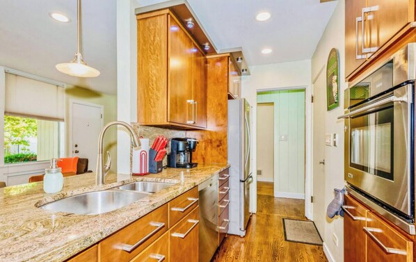 A modern kitchen with granite countertops, stainless steel appliances, wooden cabinets, and a built-in oven.