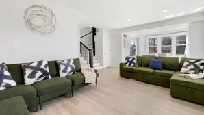 Een moderne woonkamer met twee groene banken, abstracte muurkunst en een trap naar een ander niveau.