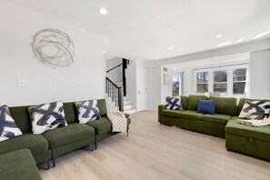 A modern living room with two green sofas, abstract wall art, and a staircase leading to another level. - Elegant 4BR Lakefront Retreat-Ready For Long-Stay (Antioch)