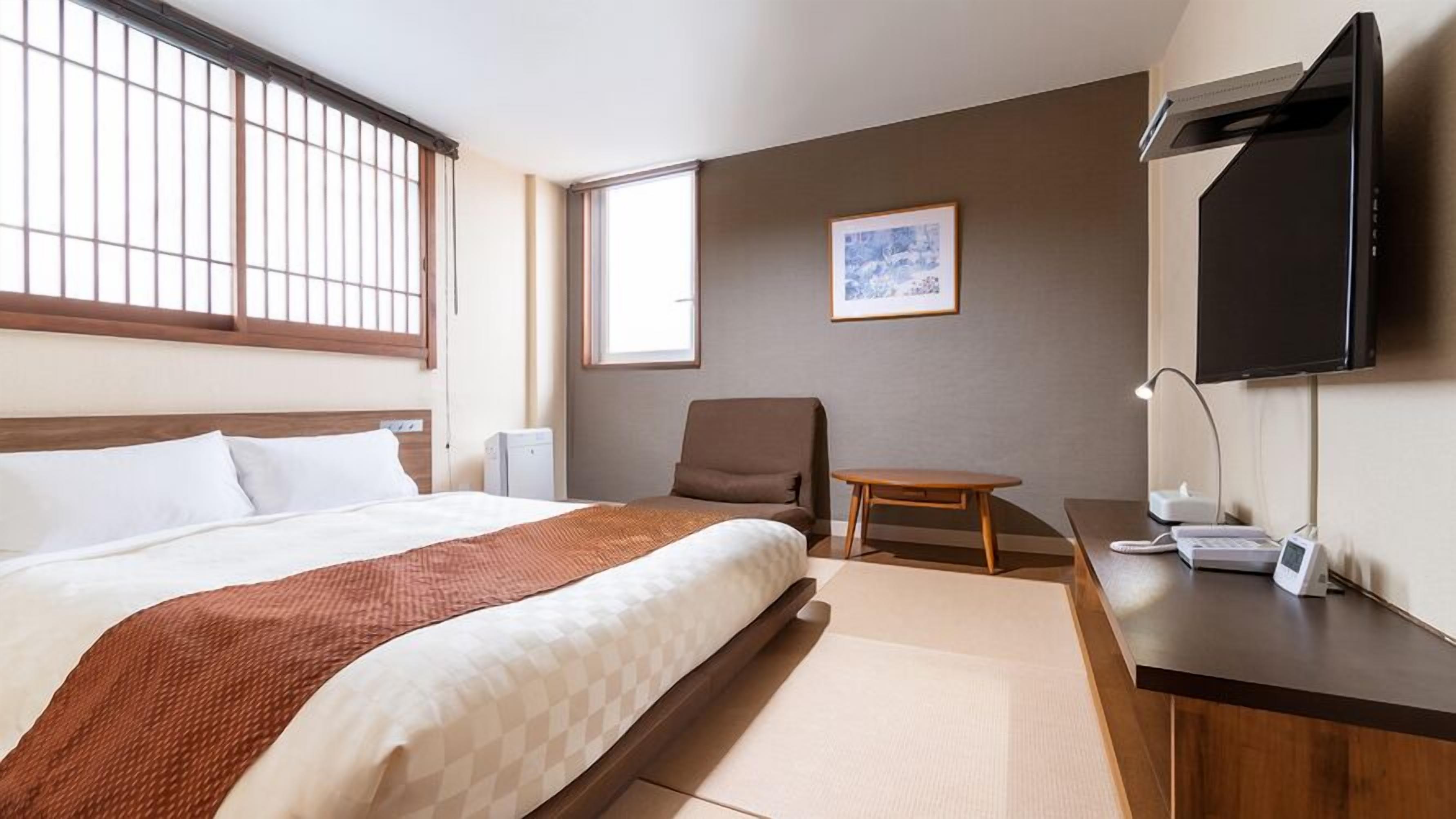 A hotel room with a bed, a desk, a chair, a TV, and a window.