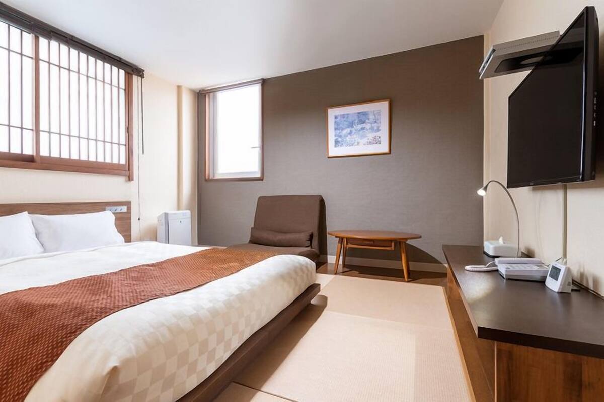 A hotel room with a bed, a desk, a chair, a TV, and a window.