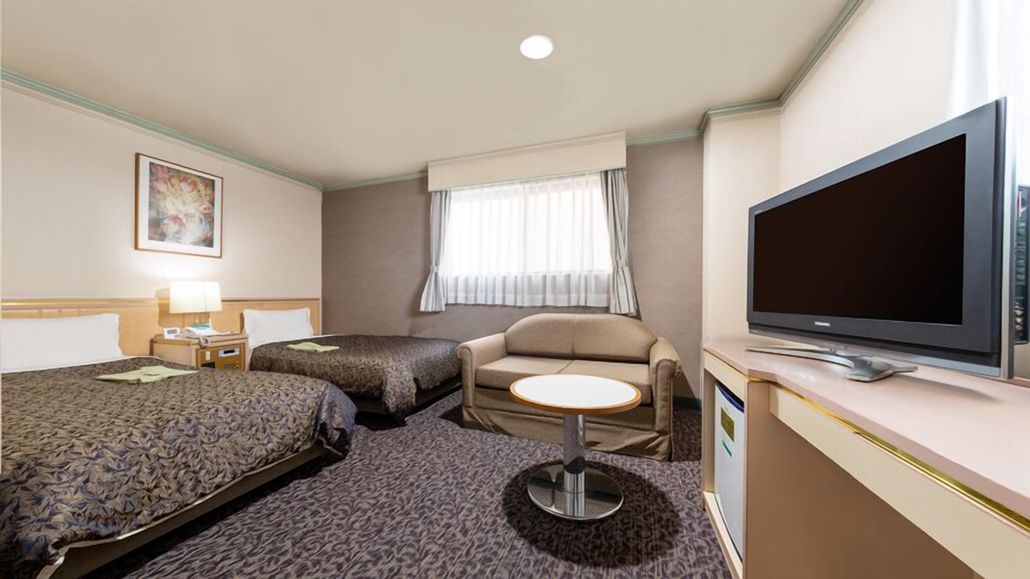 A hotel room with two beds, a sofa, a small round table, a television, and a window with curtains.