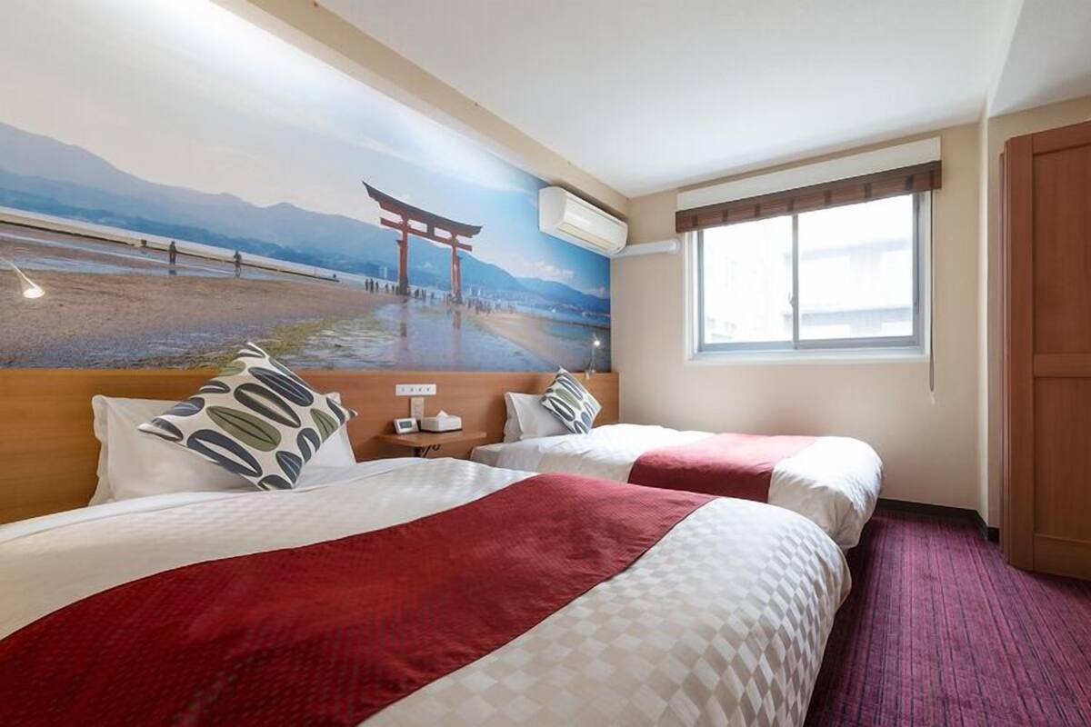 A hotel room with two beds, a mural of a torii gate, a window, and a radiator.