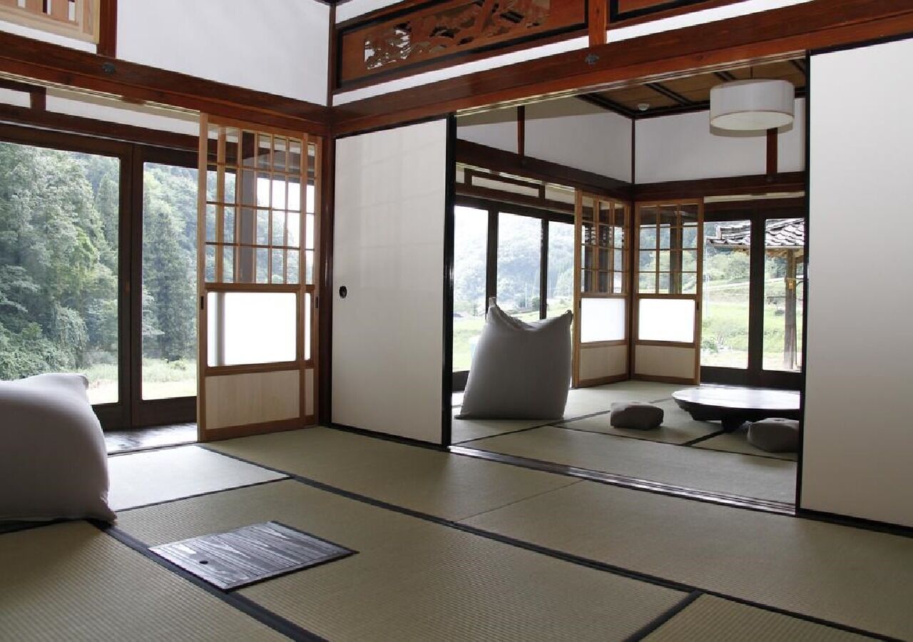 A traditional Japanese room with tatami flooring, sliding doors, and a view of a forest.