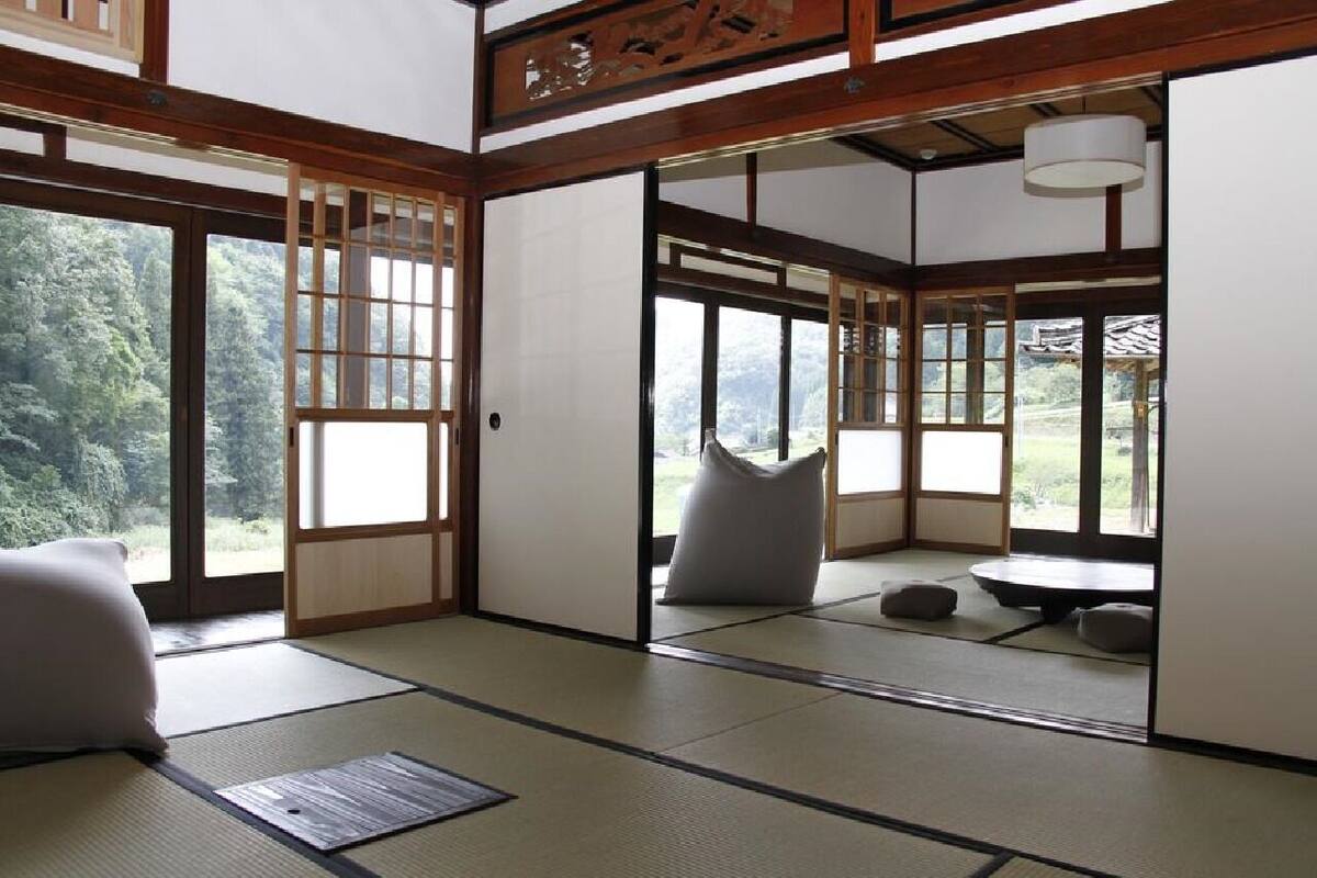 Una habitación japonesa tradicional con suelo de tatami, puertas correderas y vistas a un bosque.