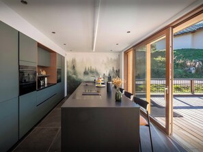 A modern kitchen with a central island, built-in appliances, and a view of a green landscape through large windows. - Chalet Artemis - Modern and bright chalet with sauna - OVO Network (Les Belleville)