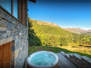 Ein Whirlpool auf einer Holzterrasse mit einer Steinmauer und Blick auf eine Berglandschaft.