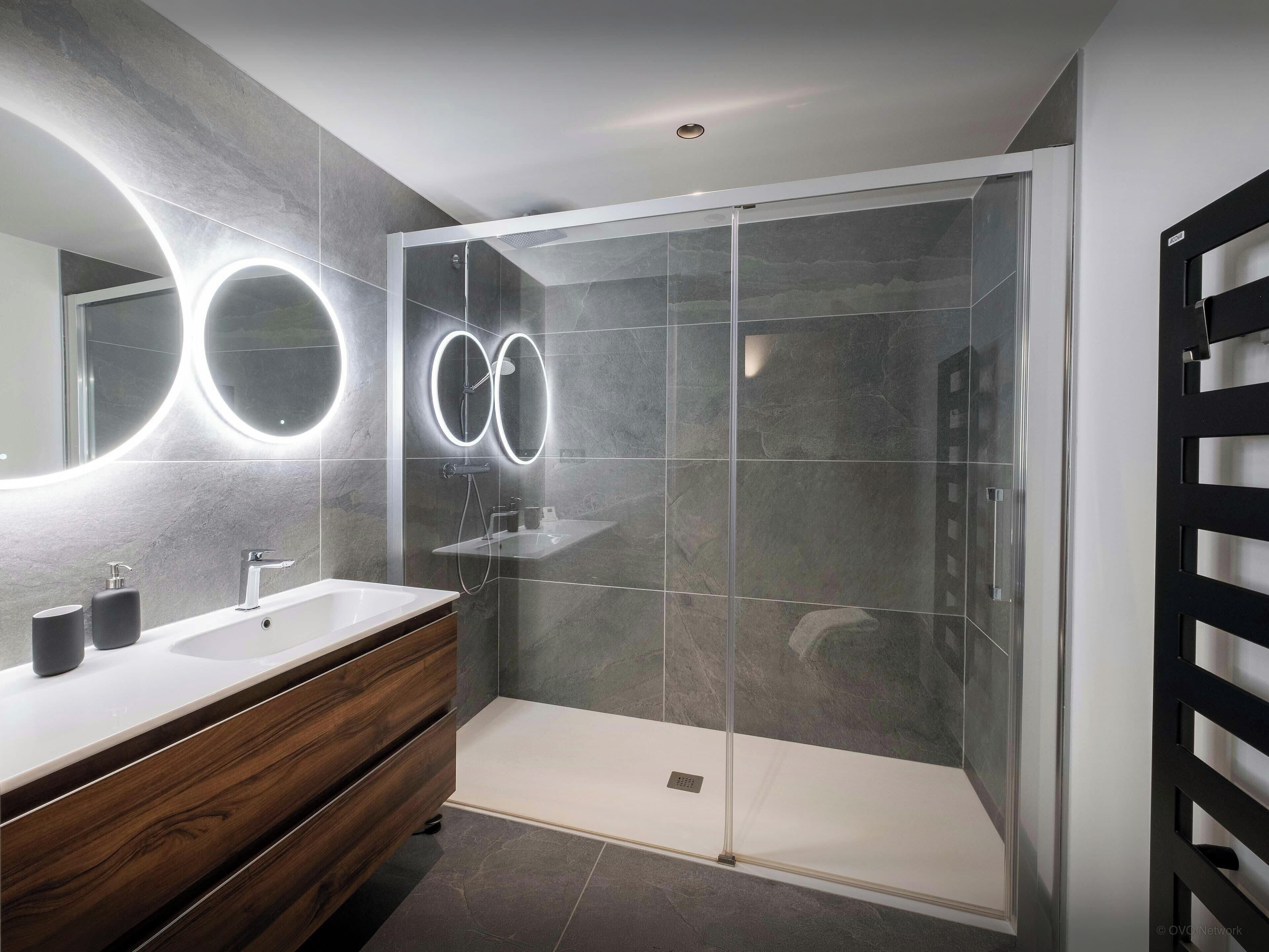 A modern bathroom with a glass-enclosed shower, a vanity with a mirror, and a wooden cabinet.