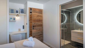 Ein modernes Schlafzimmer mit Bett, Schreibtisch, Holzschrank und einem Badezimmer mit Glasdusche.