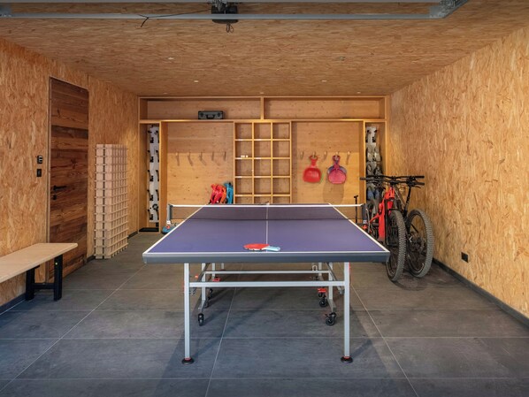 A ping pong table with wheels, a bench, and a bicycle in a room with wooden walls and a tiled floor.